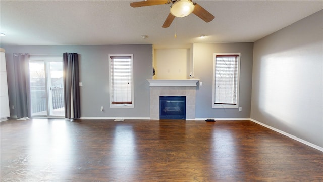 unfurnished living room featuring a tile fireplace, dark hardwood / wood-style flooring, ceiling fan, and a healthy amount of sunlight