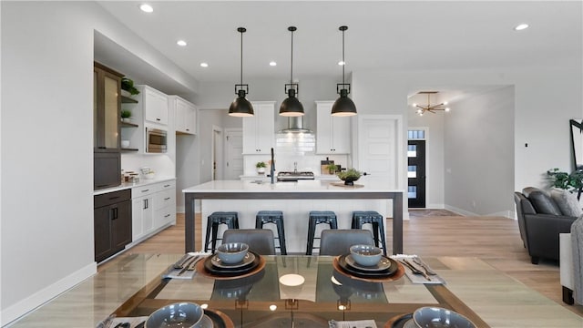 kitchen featuring white cabinets, pendant lighting, stainless steel microwave, and an island with sink