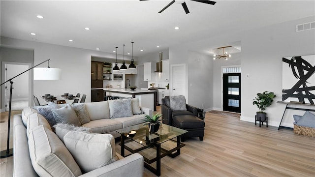 living room featuring ceiling fan with notable chandelier, light hardwood / wood-style floors, and sink