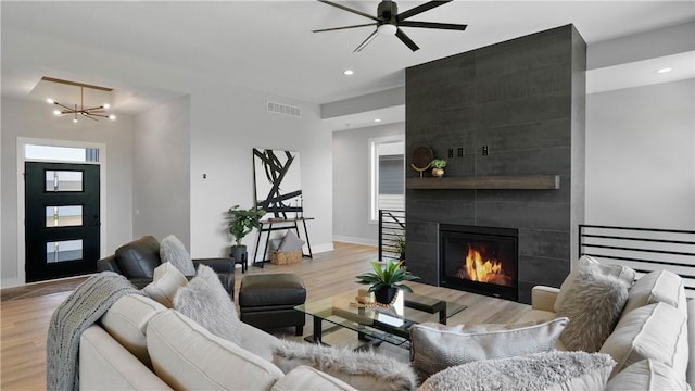 living room featuring ceiling fan with notable chandelier, light wood-type flooring, and a tiled fireplace