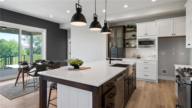 kitchen with a center island with sink, light wood-type flooring, decorative light fixtures, white cabinetry, and stainless steel appliances