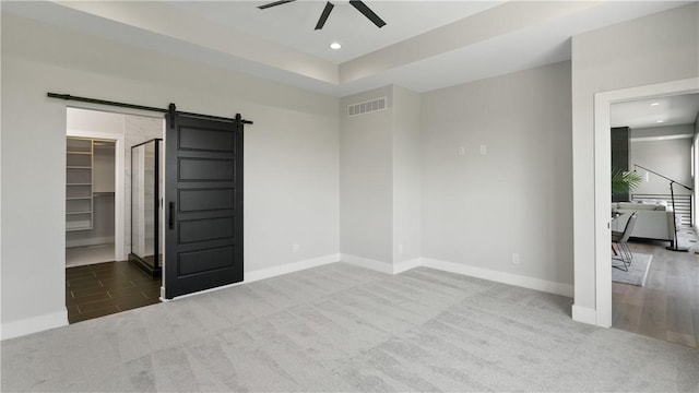 unfurnished bedroom with carpet, ceiling fan, a barn door, a spacious closet, and a closet