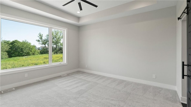 empty room with a tray ceiling, a barn door, ceiling fan, and light colored carpet