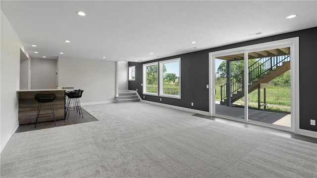 unfurnished living room with bar, light colored carpet, and plenty of natural light