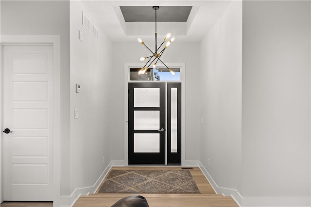 foyer entrance with a chandelier, wood-type flooring, a tray ceiling, and a wealth of natural light