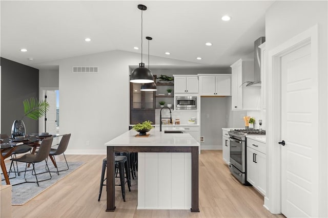 kitchen featuring wall chimney exhaust hood, stainless steel appliances, sink, a center island with sink, and white cabinets