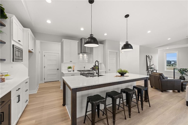 kitchen with white cabinetry, stainless steel microwave, sink, wall chimney range hood, and pendant lighting