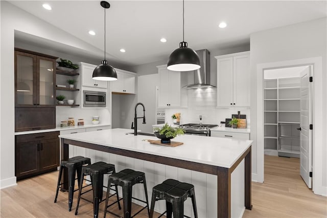 kitchen with vaulted ceiling, a kitchen island with sink, stainless steel appliances, and wall chimney range hood