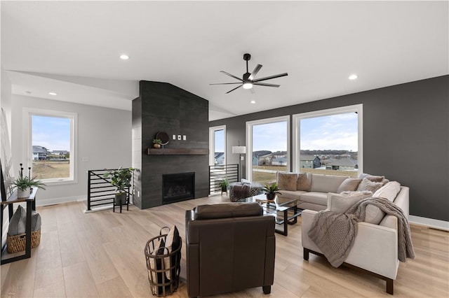 living room featuring a fireplace, light hardwood / wood-style flooring, vaulted ceiling, and ceiling fan