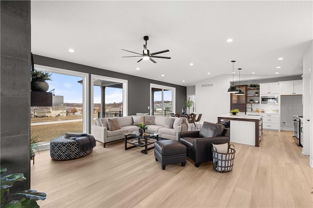 living room featuring a wealth of natural light, ceiling fan, lofted ceiling, and light wood-type flooring