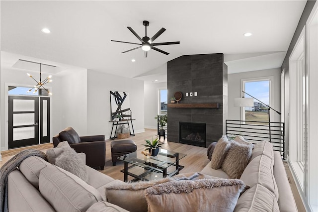 living room featuring ceiling fan with notable chandelier, light hardwood / wood-style floors, lofted ceiling, and a tiled fireplace