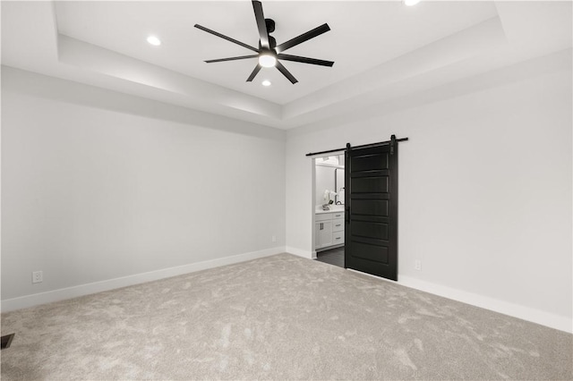 unfurnished bedroom featuring ceiling fan, a barn door, carpet floors, and a tray ceiling