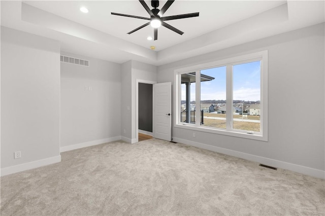 empty room with a raised ceiling, ceiling fan, and light colored carpet