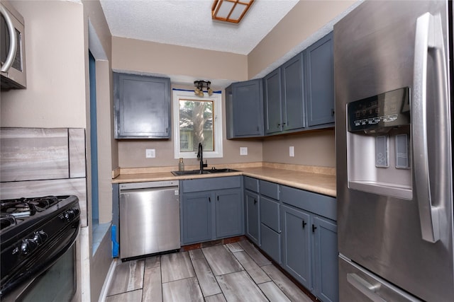 kitchen featuring blue cabinetry, appliances with stainless steel finishes, sink, and a textured ceiling