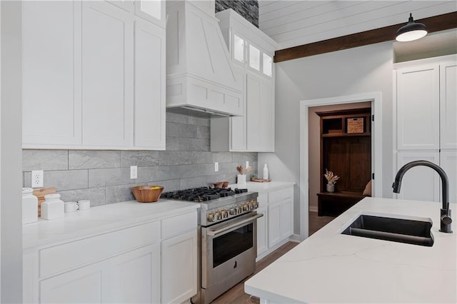 kitchen featuring backsplash, custom range hood, stainless steel stove, white cabinetry, and a sink