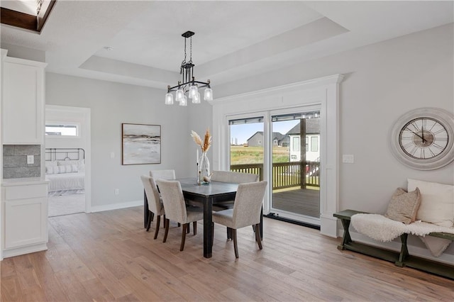 dining room featuring a raised ceiling, baseboards, light wood-type flooring, and a chandelier