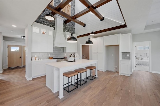 kitchen with white cabinetry, hanging light fixtures, and a center island with sink