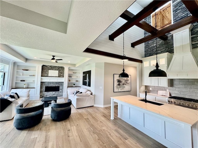 living area featuring built in shelves, a fireplace, light wood finished floors, baseboards, and ceiling fan