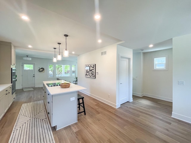 kitchen with a center island, pendant lighting, light hardwood / wood-style floors, a breakfast bar area, and white cabinets