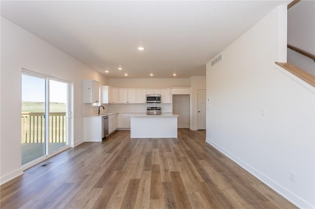 kitchen with appliances with stainless steel finishes, sink, white cabinets, light hardwood / wood-style floors, and a kitchen island