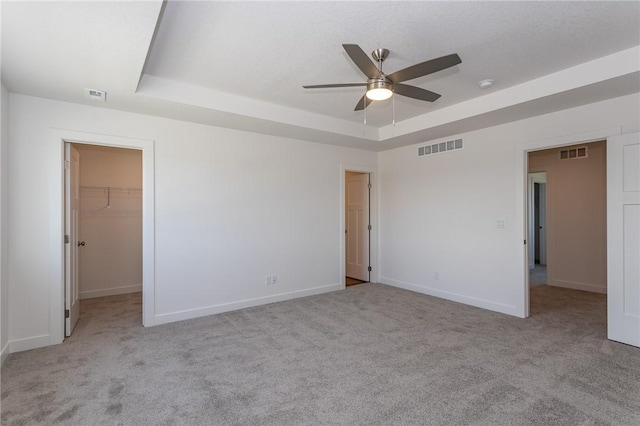 unfurnished bedroom featuring a raised ceiling, a walk in closet, ceiling fan, and a closet