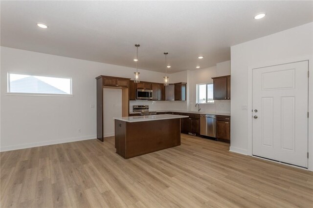 kitchen with appliances with stainless steel finishes, sink, decorative light fixtures, light hardwood / wood-style flooring, and a kitchen island