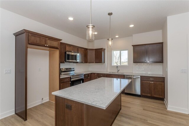 kitchen featuring light stone countertops, appliances with stainless steel finishes, decorative backsplash, sink, and a kitchen island