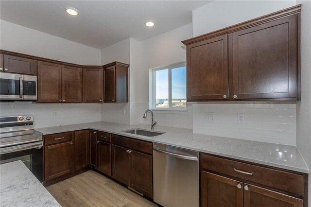 kitchen with light stone countertops, sink, light hardwood / wood-style floors, dark brown cabinets, and appliances with stainless steel finishes