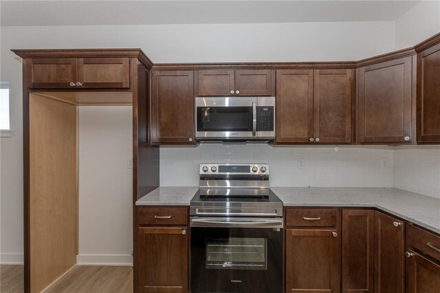 kitchen with light stone countertops, backsplash, appliances with stainless steel finishes, and light hardwood / wood-style flooring