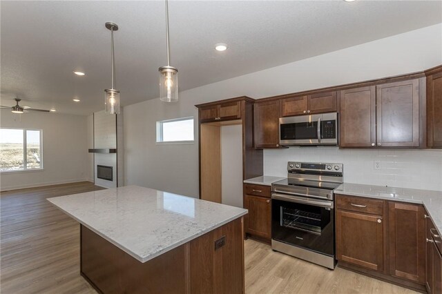 kitchen with a center island, ceiling fan, decorative backsplash, light stone countertops, and appliances with stainless steel finishes