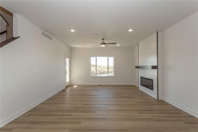 unfurnished living room with ceiling fan, a large fireplace, and light hardwood / wood-style floors