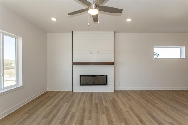 unfurnished living room with a large fireplace, light hardwood / wood-style floors, and ceiling fan