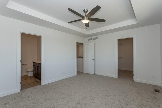 unfurnished bedroom with a raised ceiling, ensuite bath, ceiling fan, a spacious closet, and a closet