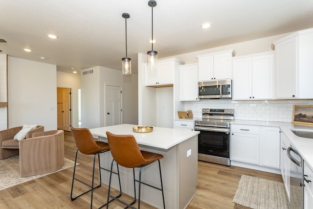 985 11th St, Waukee, IA 50263 - kitchen with visible vents, light wood finished floors, backsplash, a center island, and appliances with stainless steel finishes