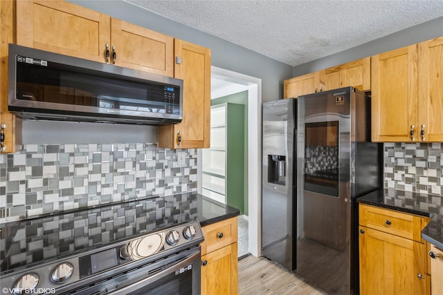 kitchen featuring dark stone counters, decorative backsplash, light wood-type flooring, a textured ceiling, and stainless steel appliances