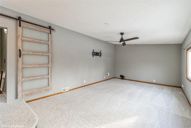 empty room with ceiling fan, a barn door, carpet floors, and a textured ceiling