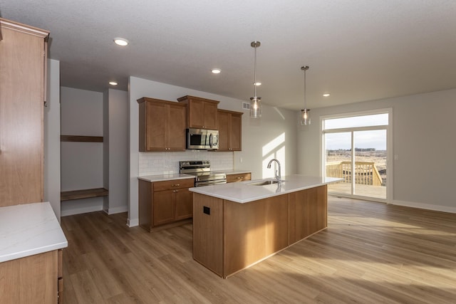 kitchen with stainless steel appliances, backsplash, brown cabinetry, a sink, and light wood-type flooring