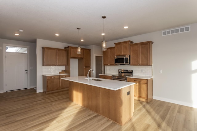 kitchen with a sink, visible vents, appliances with stainless steel finishes, light wood-type flooring, and brown cabinetry