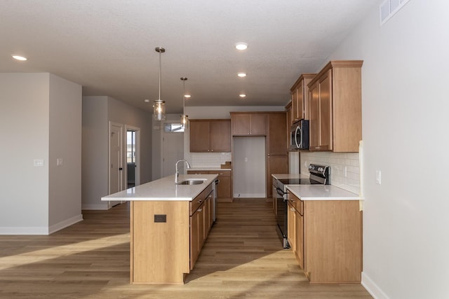 kitchen featuring decorative backsplash, an island with sink, appliances with stainless steel finishes, light wood-type flooring, and a sink