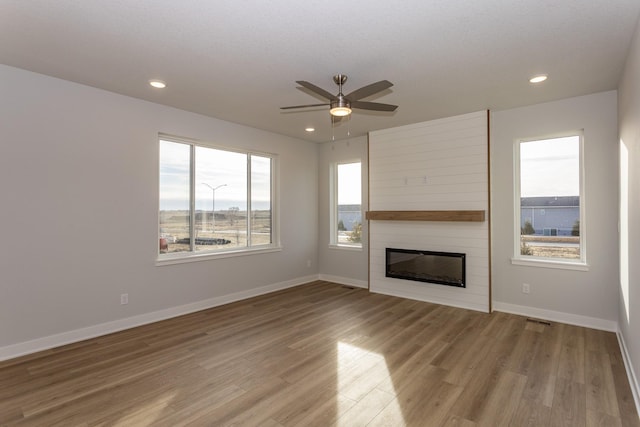 unfurnished living room with baseboards, a large fireplace, recessed lighting, and light wood-style floors