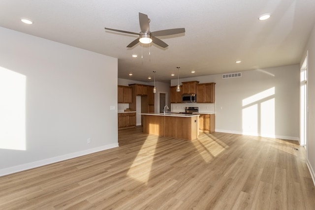 kitchen with brown cabinets, stainless steel appliances, light countertops, light wood-style floors, and open floor plan