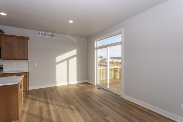 kitchen featuring light countertops, visible vents, decorative backsplash, light wood-style floors, and baseboards