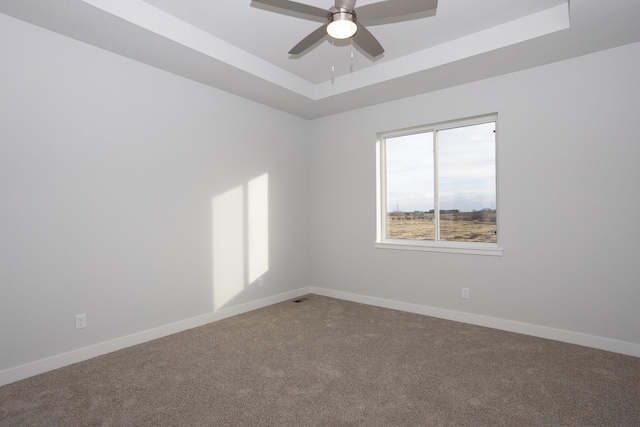 carpeted spare room with ceiling fan, a tray ceiling, and baseboards