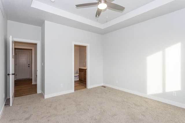 unfurnished bedroom with carpet, a raised ceiling, connected bathroom, and baseboards