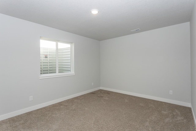 spare room featuring carpet floors, visible vents, a textured ceiling, and baseboards