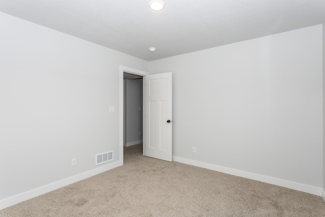 empty room with visible vents, light carpet, and baseboards