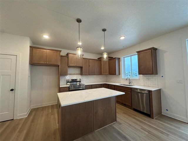 kitchen with a center island, sink, light stone countertops, decorative light fixtures, and stainless steel appliances