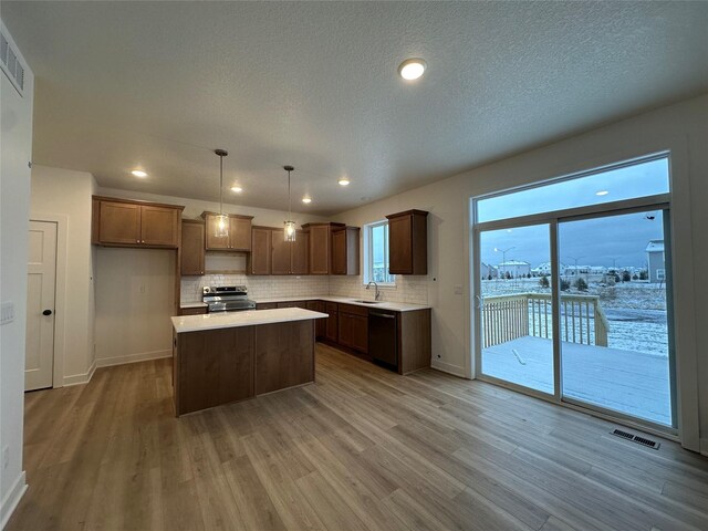 kitchen with pendant lighting, stainless steel range with electric cooktop, sink, black dishwasher, and a kitchen island