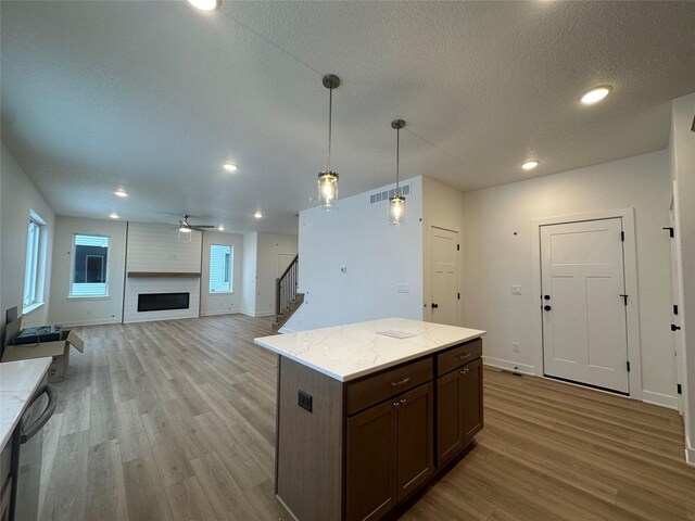 kitchen with light wood-type flooring, light stone counters, ceiling fan, a fireplace, and hanging light fixtures