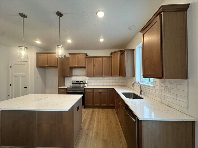 kitchen with light stone countertops, stainless steel appliances, sink, pendant lighting, and light hardwood / wood-style floors